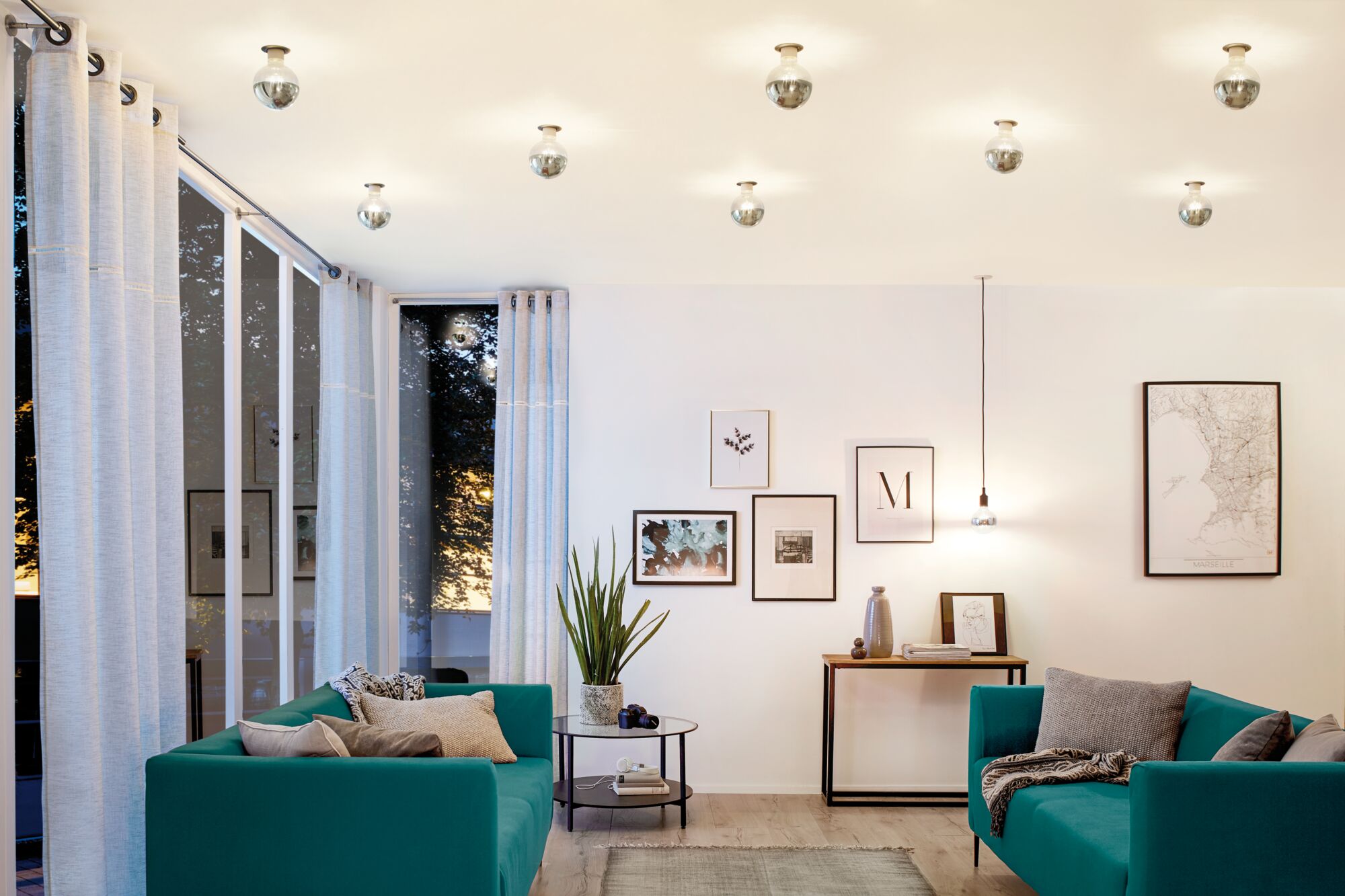 Salon moderne avec deux canapés turquoise, éclairage minimaliste au plafond et tableaux encadrés.