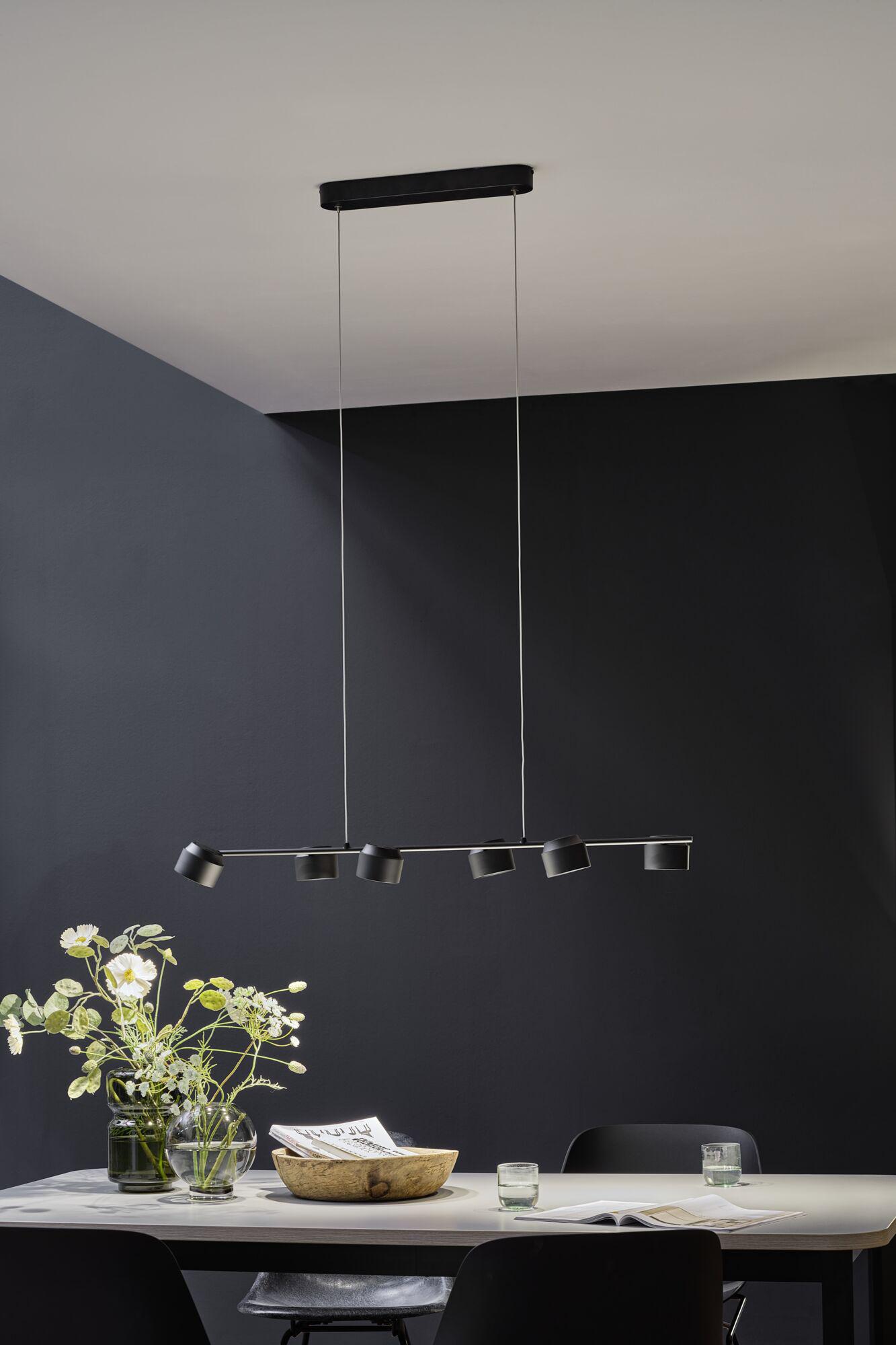Modern black LED pendant light with six spotlights above dining table with decor and chairs.
