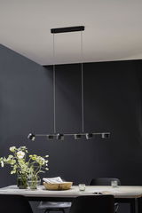 Moderne zwarte LED-hanglamp met zes spots boven eettafel met decoratie en stoelen.