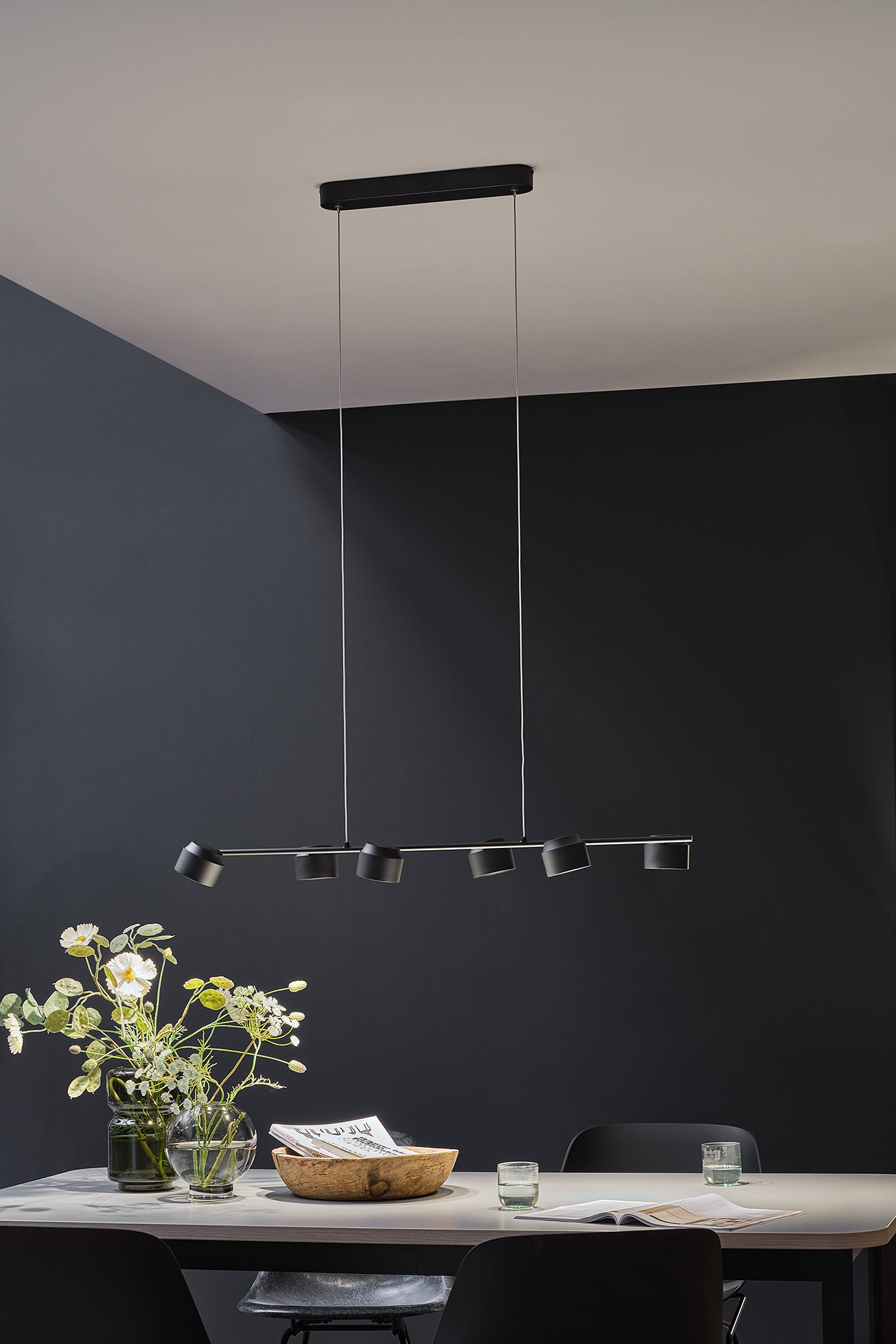 Schwarze LED-Deckenleuchte mit sechs verstellbaren Spots über modernem Esstisch mit Dekoration