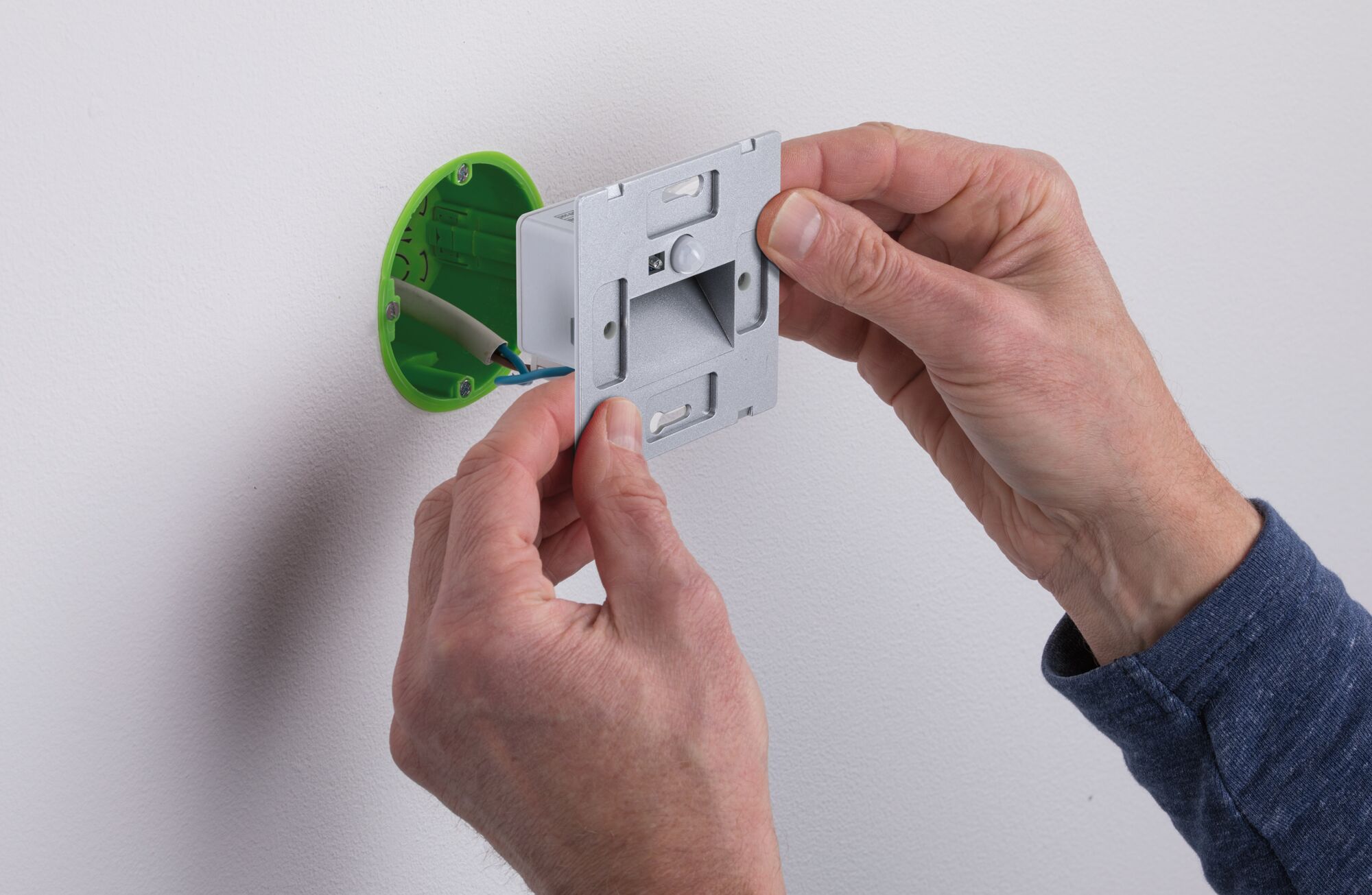 Installation of silver LED wall recessed light with green plastic housing on white wall