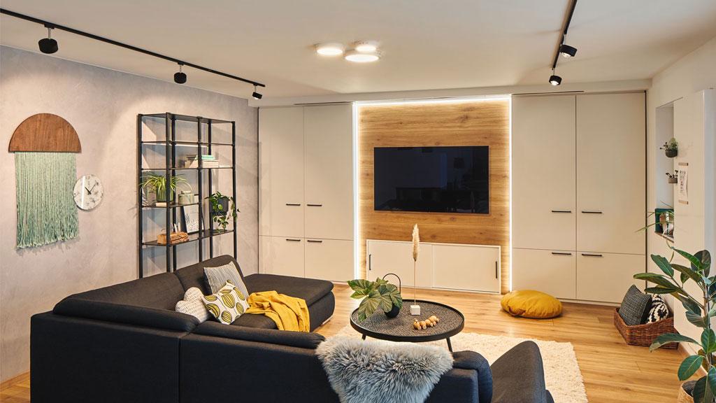 Moderne woonkamer met zwarte hoekbank, houten tv-wand en LED-verlichting voor een gezellige sfeer.