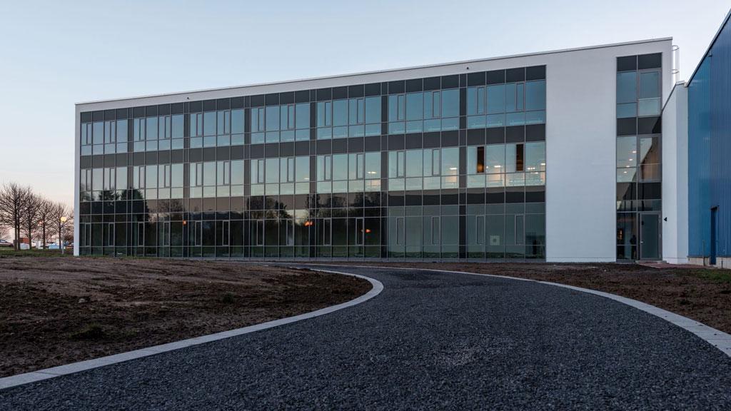 Modernes Bürogebäude mit großer Glasfassade und geschwungenem Asphaltweg im Vordergrund bei Dämmerung.