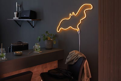 Warm orange LED neon light in abstract shape on dark wall in modern living space with bar counter.