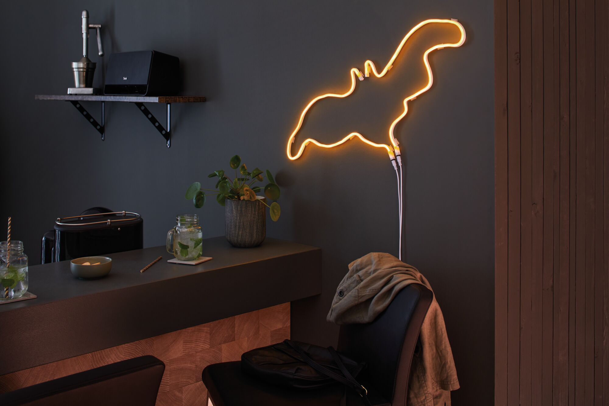 Warmes orangefarbenes LED-Neonlicht in abstrakter Form an dunkler Wand im modernen Wohnraum mit Bar.