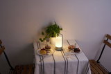 Moderne draagbare witte LED-tafellamp op gedekte tafel met gebak en groene plant.