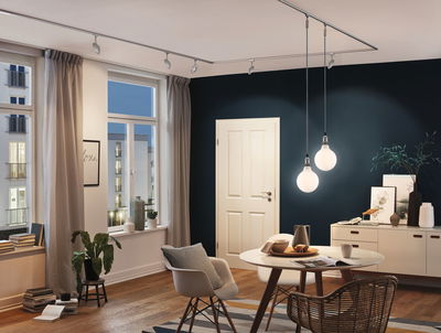 Modern dining room with white pendant lights, wooden floor, and dark blue wall for ambient lighting.