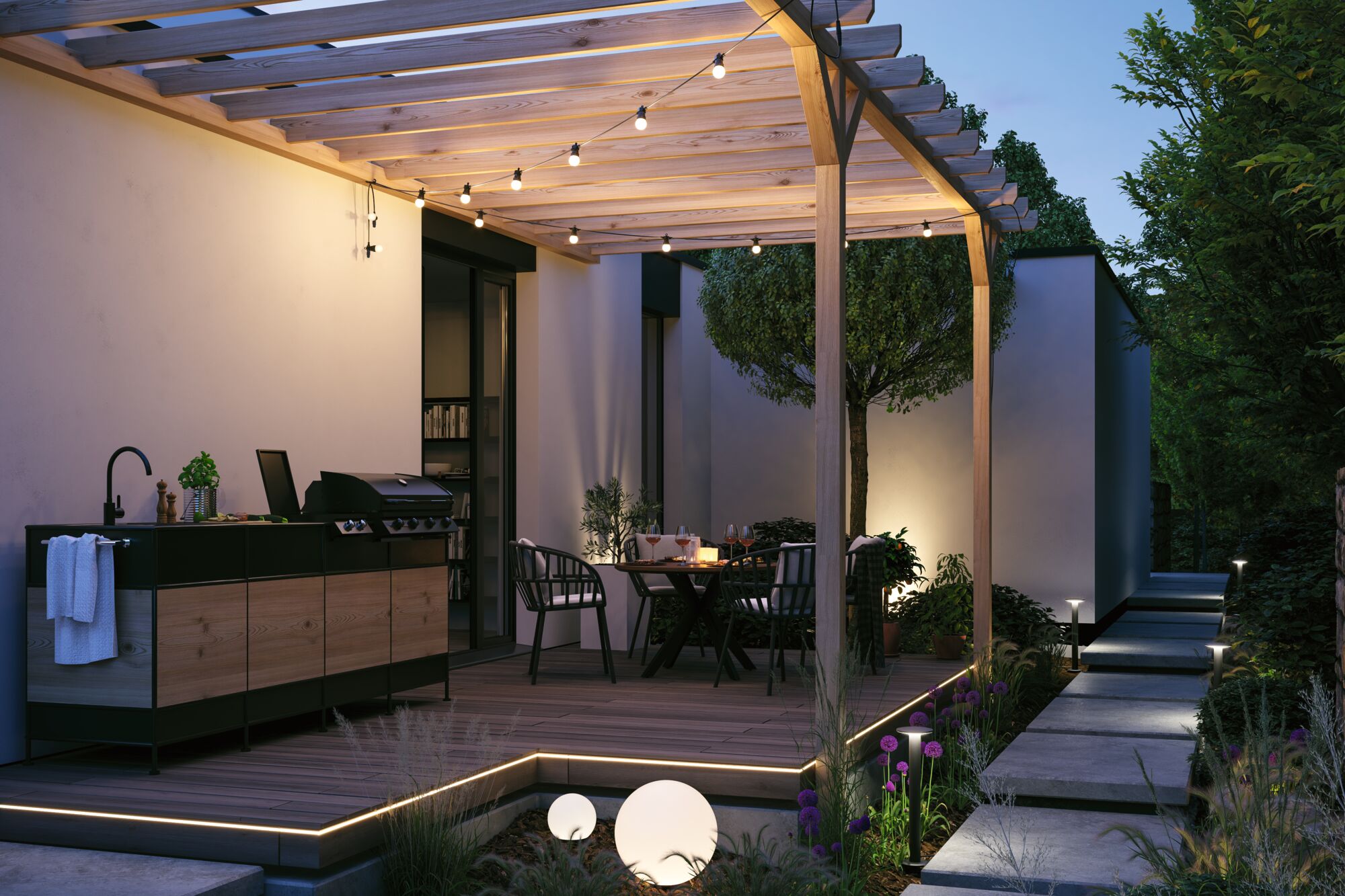 Modern outdoor kitchen with wood panels and black countertop under lit pergola with garden furniture