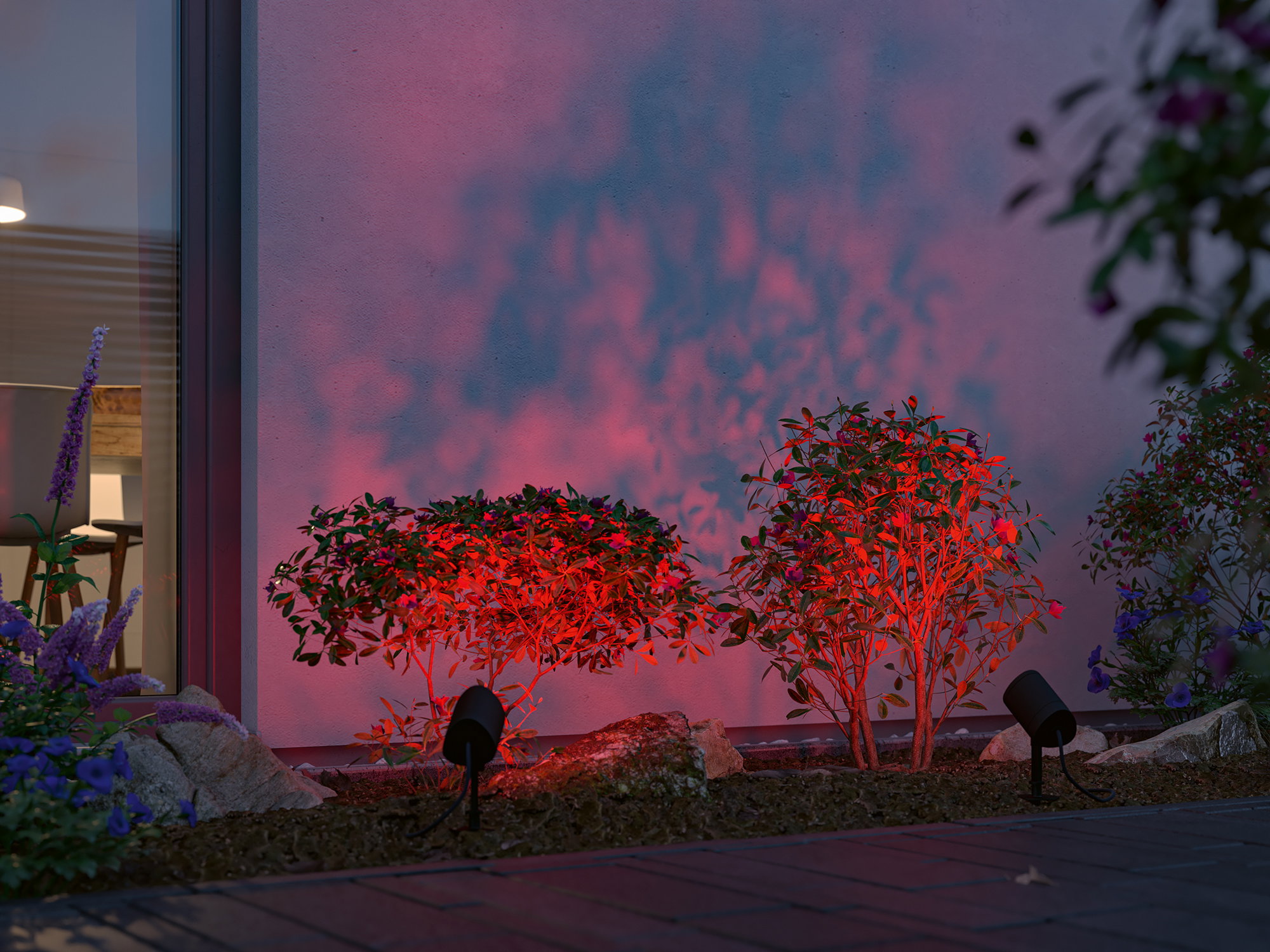 Two black LED garden spotlights illuminate red plants against an exterior house wall