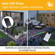 Solar LED strips with black solar panel and remote control on garden terrace with plants and outdoor furniture