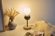Modern table lamp with wooden base and black metal stem, frosted glass globe emits warm light indoors.