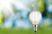 LED-Glühbirne mit transparentem Glas und silberner Fassung vor grün-blauem Hintergrund