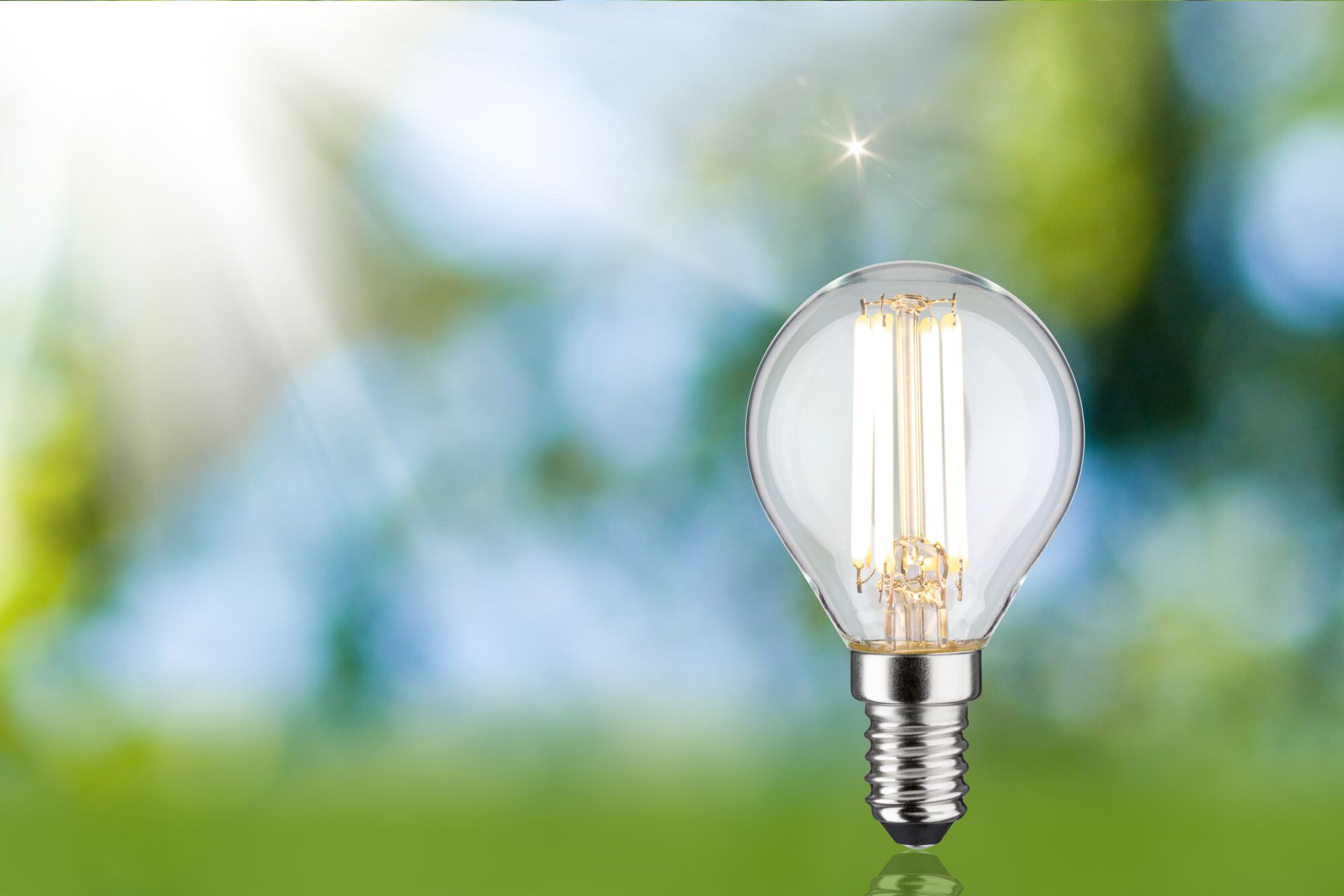 LED-lamp met helder glas en zilveren voet tegen een groene en blauwe wazige achtergrond