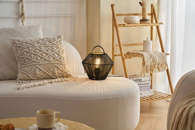Black woven table lamp on cream sofa with macrame cushion in cozy living room setting