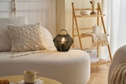 Schwarze Tischlampe aus geflochtenem Material auf beigem Sofa mit Makramee-Kissen im Wohnzimmer