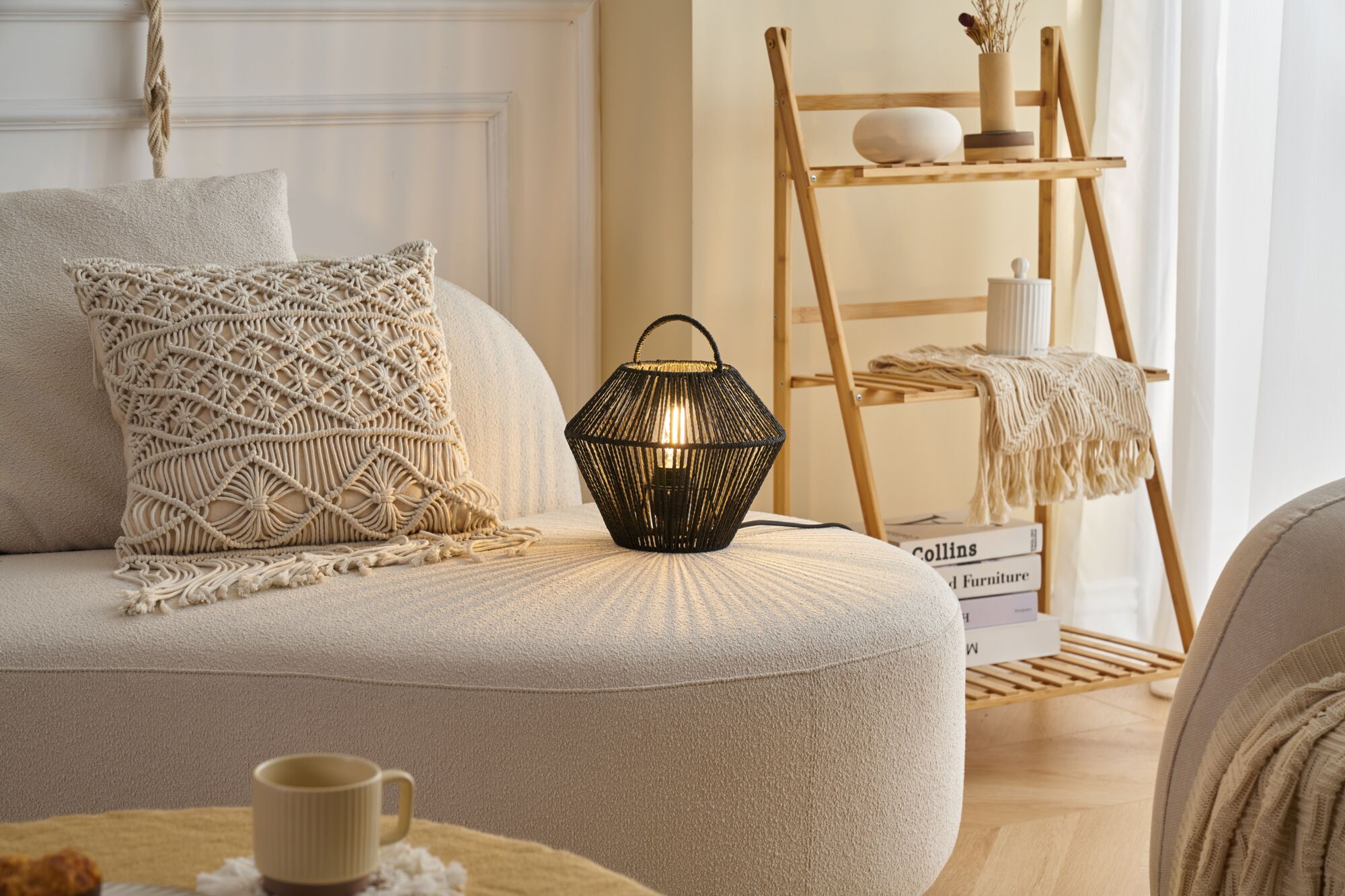 Schwarze Tischlampe aus geflochtenem Material auf beigem Sofa mit Makramee-Kissen im Wohnzimmer