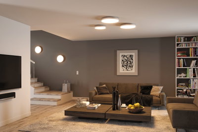 Salon moderne avec canapés marron, table basse en bois et plafonniers ronds diffusant une lumière blanc chaud.