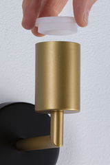 Hand hält weißen Diffusor über goldfarbenem Metall-Wandleuchter mit schwarzer Wandhalterung