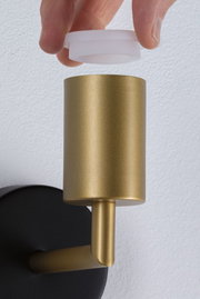 Hand hält weißen Diffusor über goldfarbenem Metall-Wandleuchter mit schwarzer Wandhalterung