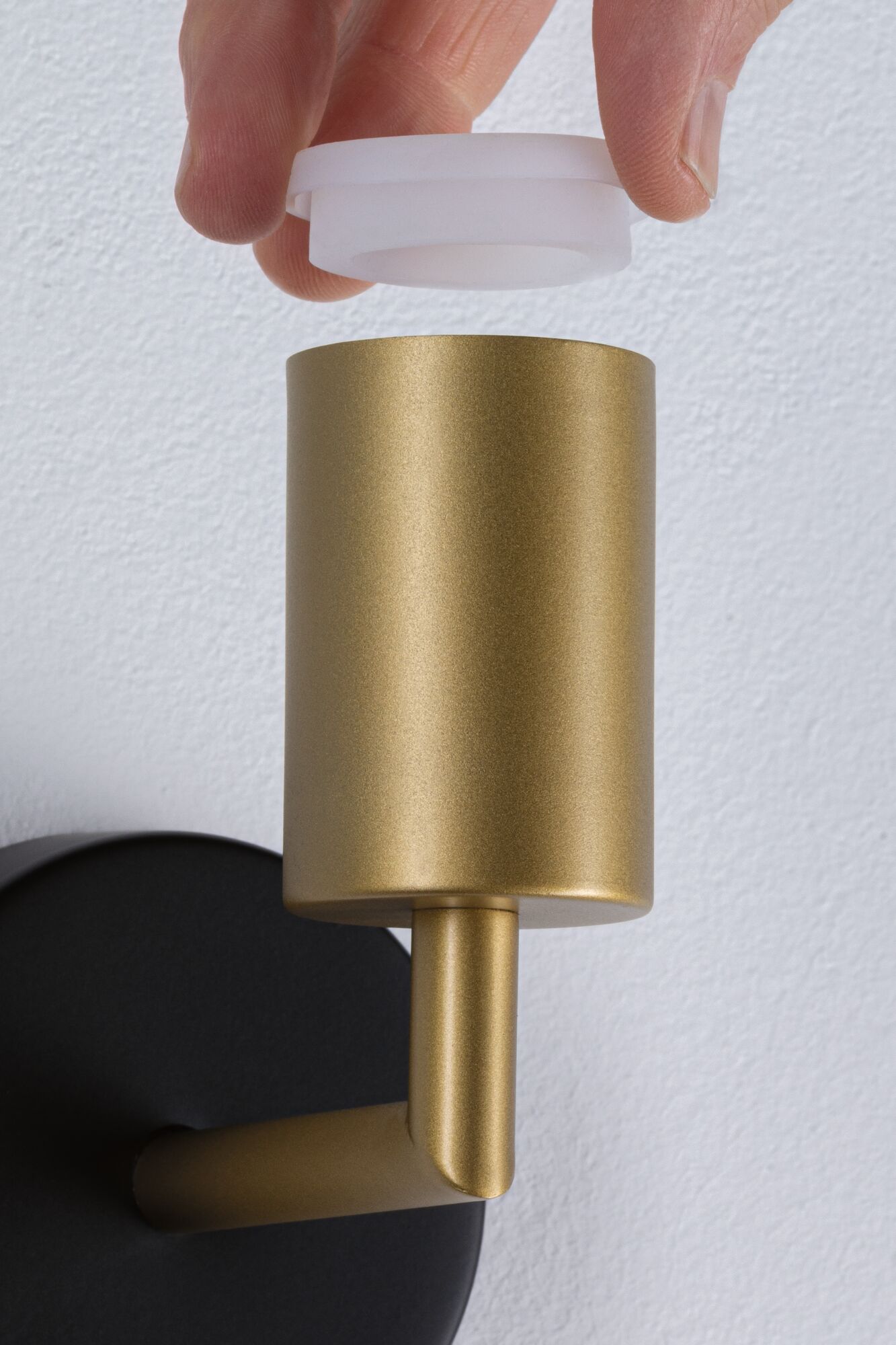 Hand hält weißen Diffusor über goldfarbenem Metall-Wandleuchter mit schwarzer Wandhalterung