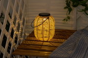 Warm light from round solar lantern made of woven natural material on wooden bench outdoors