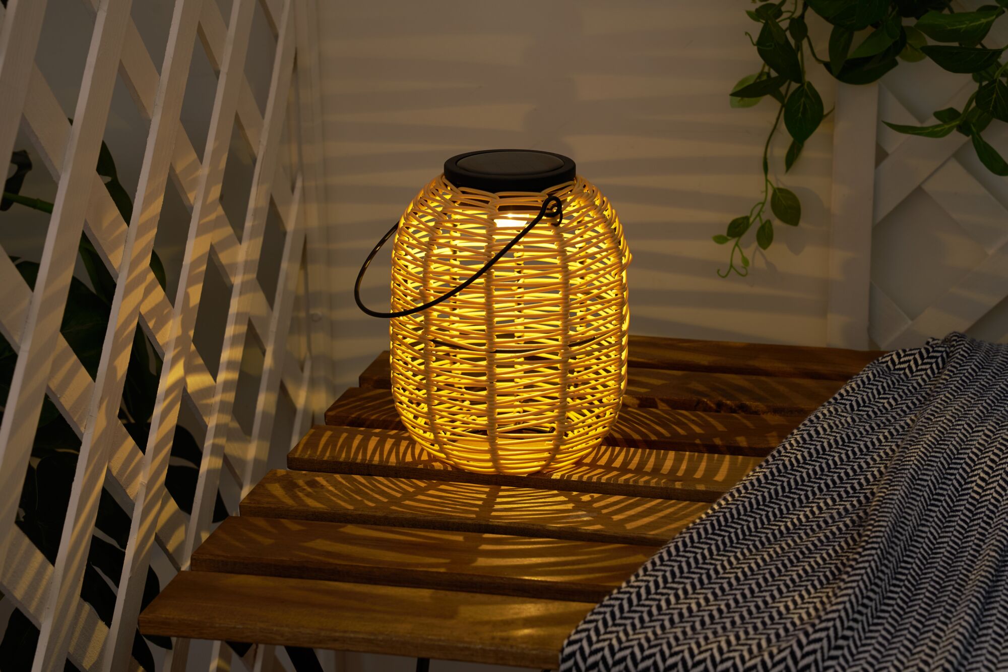 Warm light from round solar lantern made of woven natural material on wooden bench outdoors