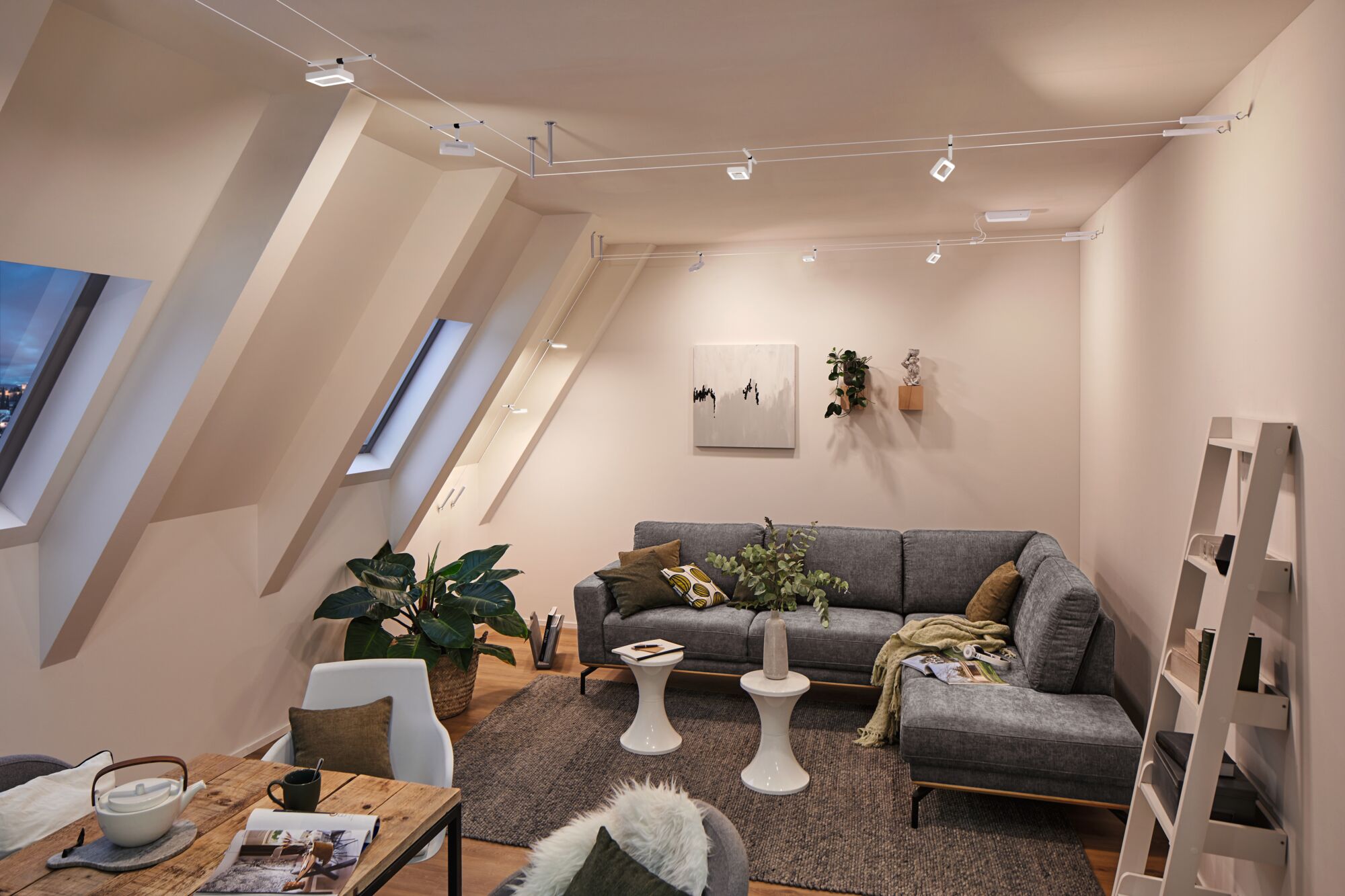 Moderne woonkamer met grijze stoffen bank, witte bijzettafels en Paulmann LED-kabelverlichting aan het plafond