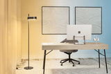 Modern black floor lamp with rectangular light head in minimalist office with wooden desk and computer.