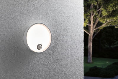 Round white outdoor wall light with motion sensor on grey wall for garden lighting.