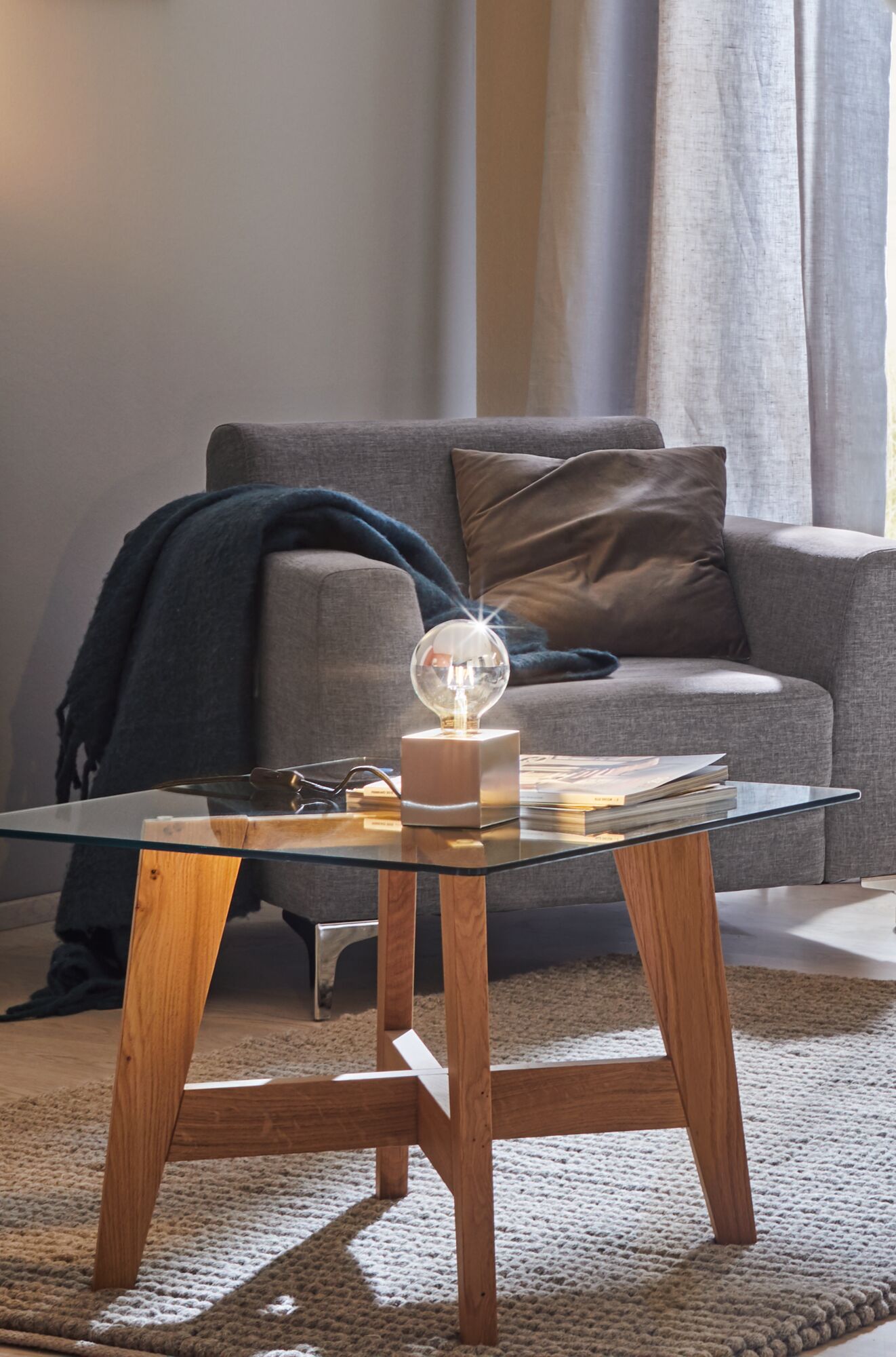 Moderner Beistelltisch mit Glasplatte und Holzgestell, dekoriert mit Glühbirne und Zeitschriften im Wohnzimmer.