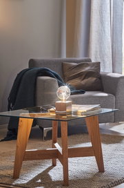 Moderner Beistelltisch mit Glasplatte und Holzgestell, dekoriert mit Glühbirne und Zeitschriften im Wohnzimmer.