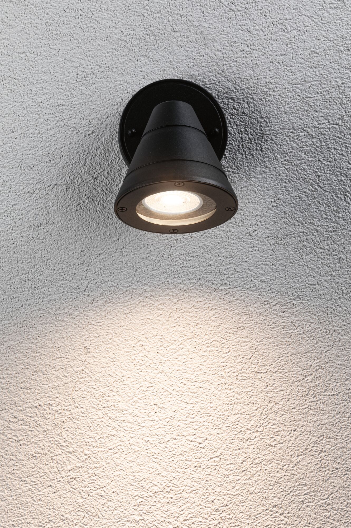 Black metal outdoor wall light with warm white LED illumination on textured wall surface