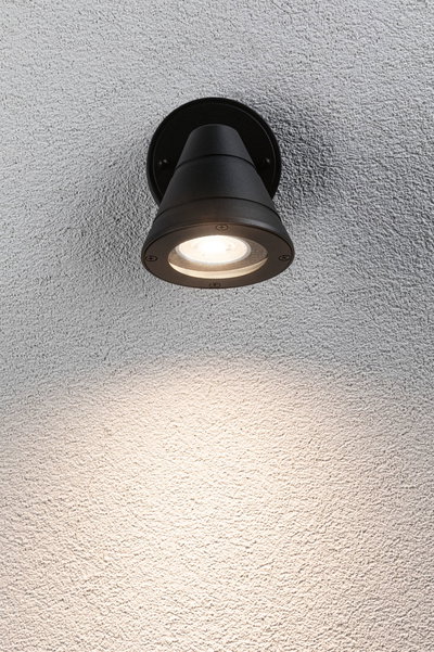 Black metal outdoor wall light with warm white LED illumination on textured wall surface