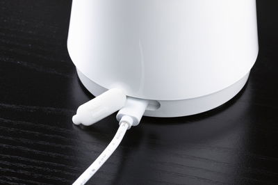 White electronic device with connected cable on black wooden surface, close-up of the connection.