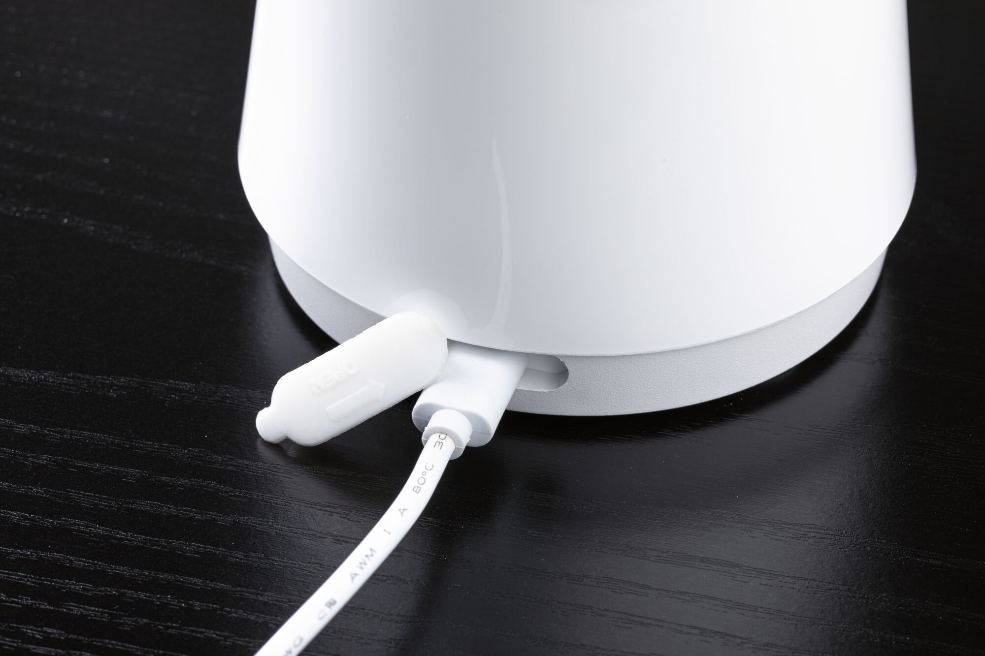 Weißes elektrisches Gerät mit angeschlossenem Kabel auf schwarzer Holzoberfläche, Nahaufnahme des Anschlusses.