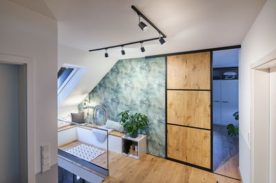 Modern attic with wooden floor, wood-look sliding door, green patterned wall, plants, and cozy bench seating.