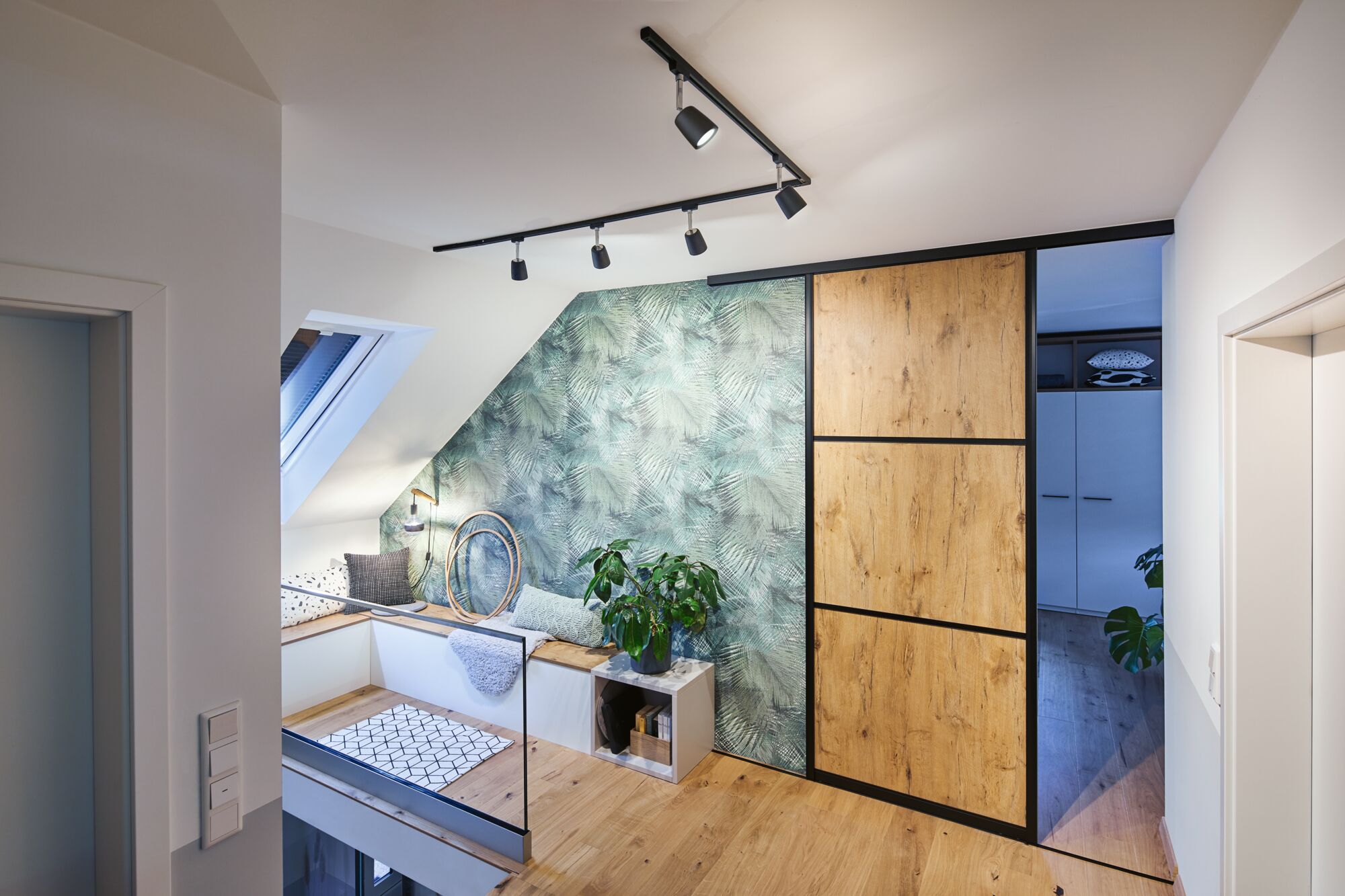Modern attic with wooden floor, wood-look sliding door, green patterned wall, plants, and cozy bench seating.