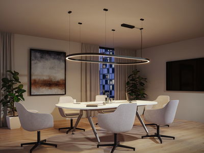 Modern round black LED pendant light above white conference table with grey chairs in office room.