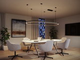 Modern round black LED pendant light above white conference table with grey chairs in office room.