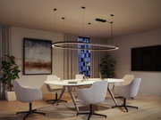 Modern round black LED pendant light above white conference table with grey chairs in office room.