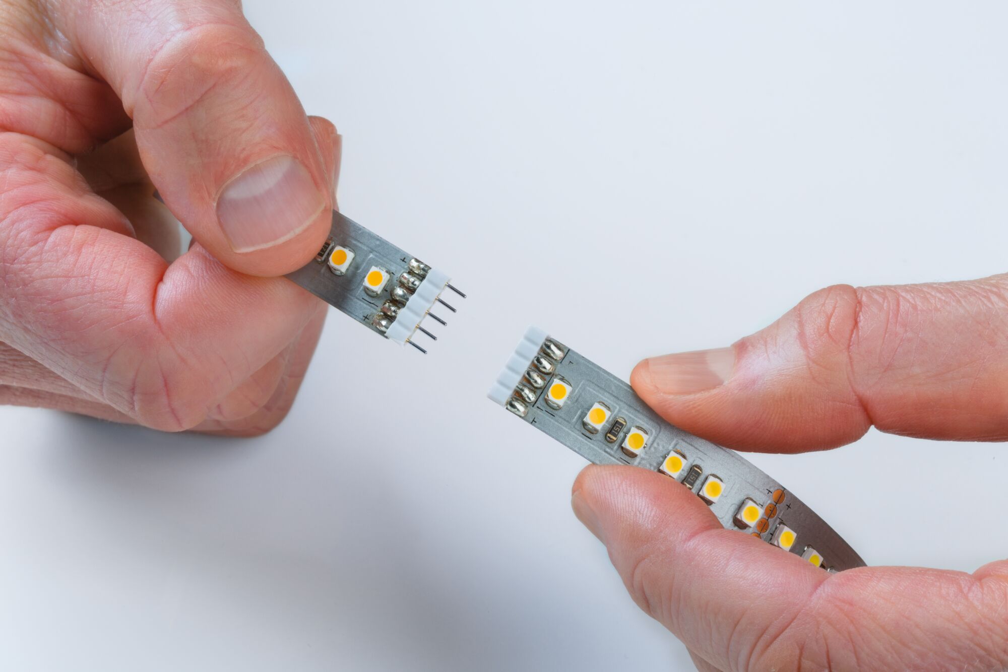 Two hands connecting LED strip with yellow LEDs on gray base for flexible lighting solution