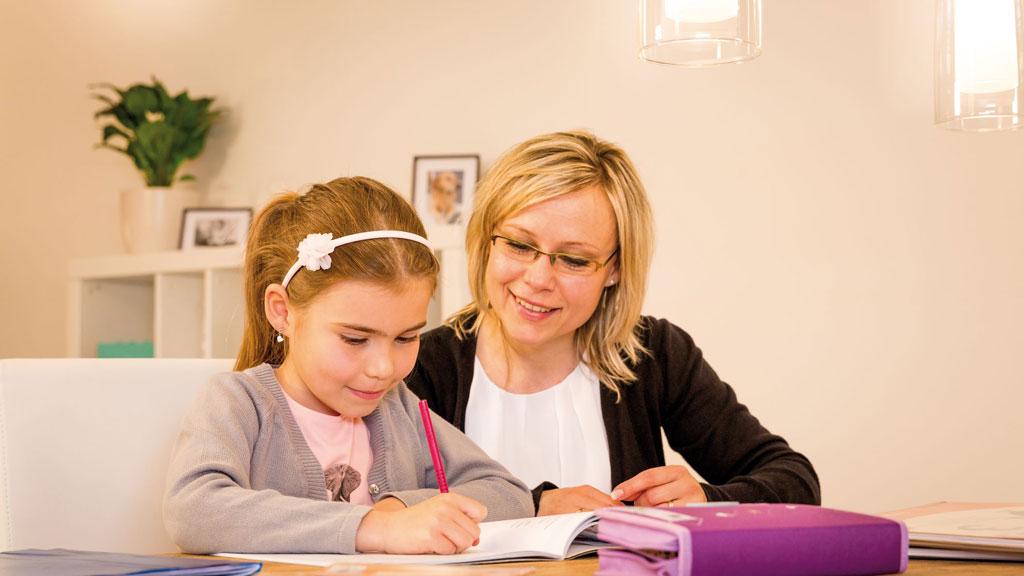 Child and woman at table with books in bright living room featuring modern lighting fixtures.