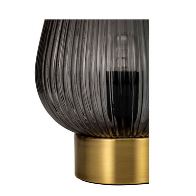 Close-up of a table lamp with ribbed smoked glass and gold metal base for elegant lighting decor.