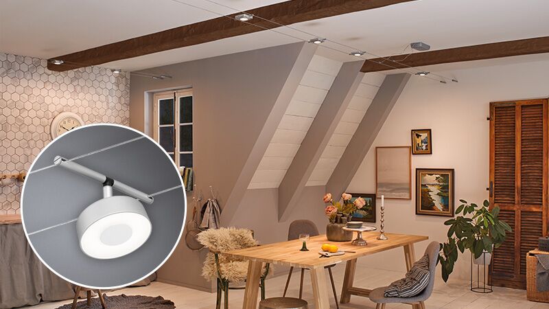 Spot sur câble moderne chromé mat avec tête LED ronde dans une salle à manger chaleureuse.