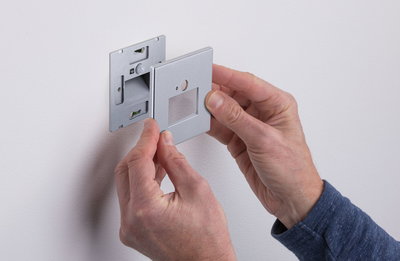 Montage van zilveren metalen wandplaat met vierkante uitsparing op witte muur voor lichtregeling