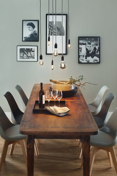 Houten eettafel met zes grijze stoelen en LED filament rookglas lampen erboven hangend.