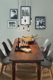 Table à manger en bois avec six chaises grises et ampoules LED filament en verre fumé suspendues.