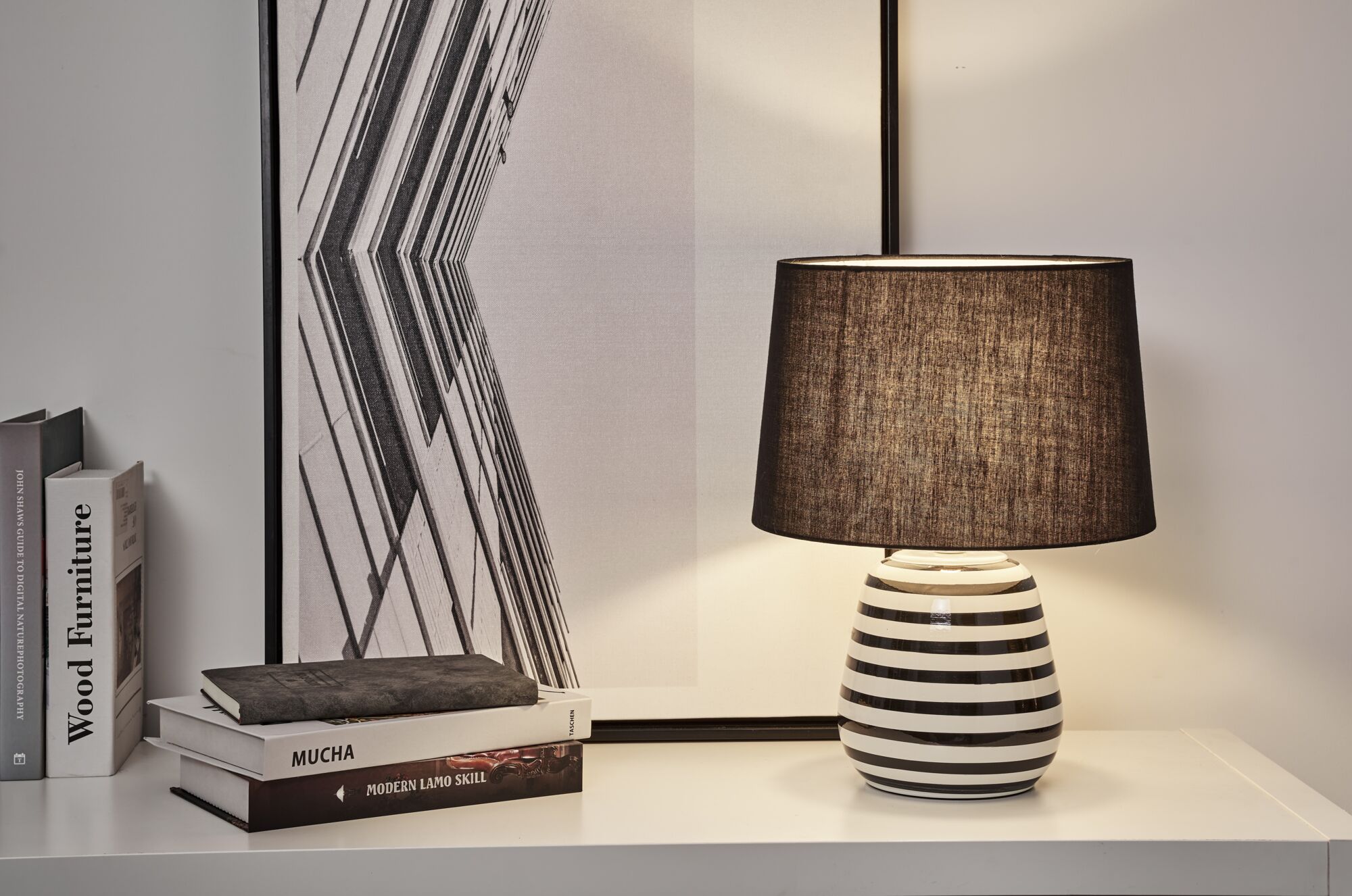 Moderne bordlampe med sort-hvid stribet keramisk fod og sort stofskærm på hvidt bord.