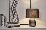 Modern table lamp with black and white striped ceramic base and black fabric shade on white table.