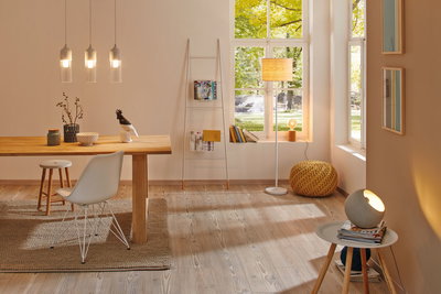 Salon lumineux avec sol en bois, lampadaire et suspensions modernes blanches et bois, design scandinave.